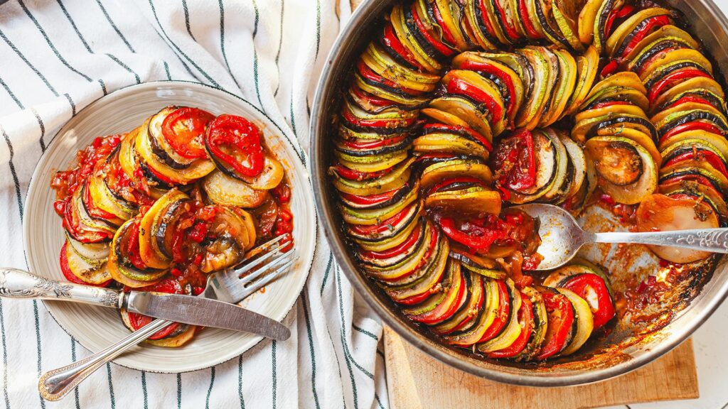 The spiraled tones of vegetables layered in a Ratatouille with a small plate to the left with a serve of it