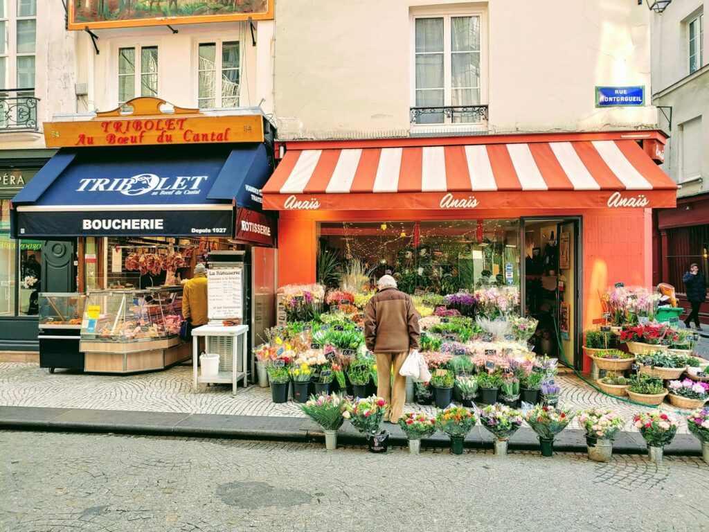 An older man browsing buckets of flowers outside a florist in France