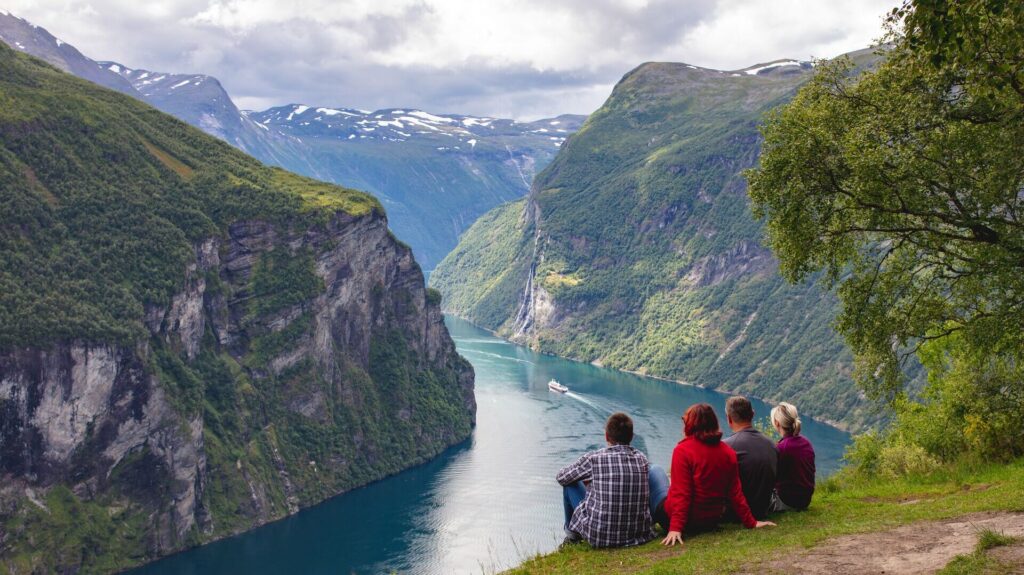 Four people sitting on the edge of a cliff looking at Geirangerfjord, Norway