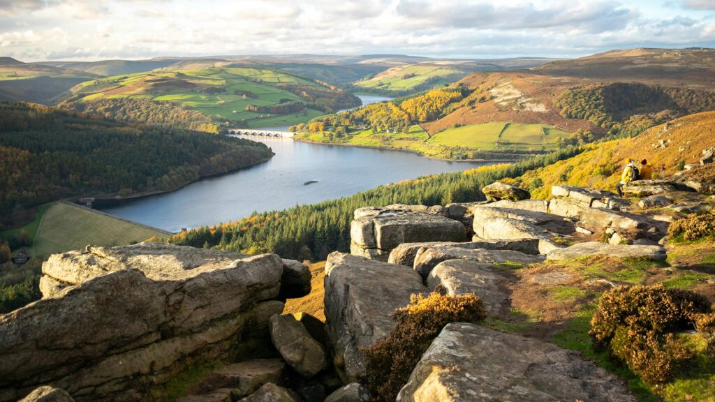 Landscape photo of the rolling patchwork hills of Peak District National Park with a bridge over a river