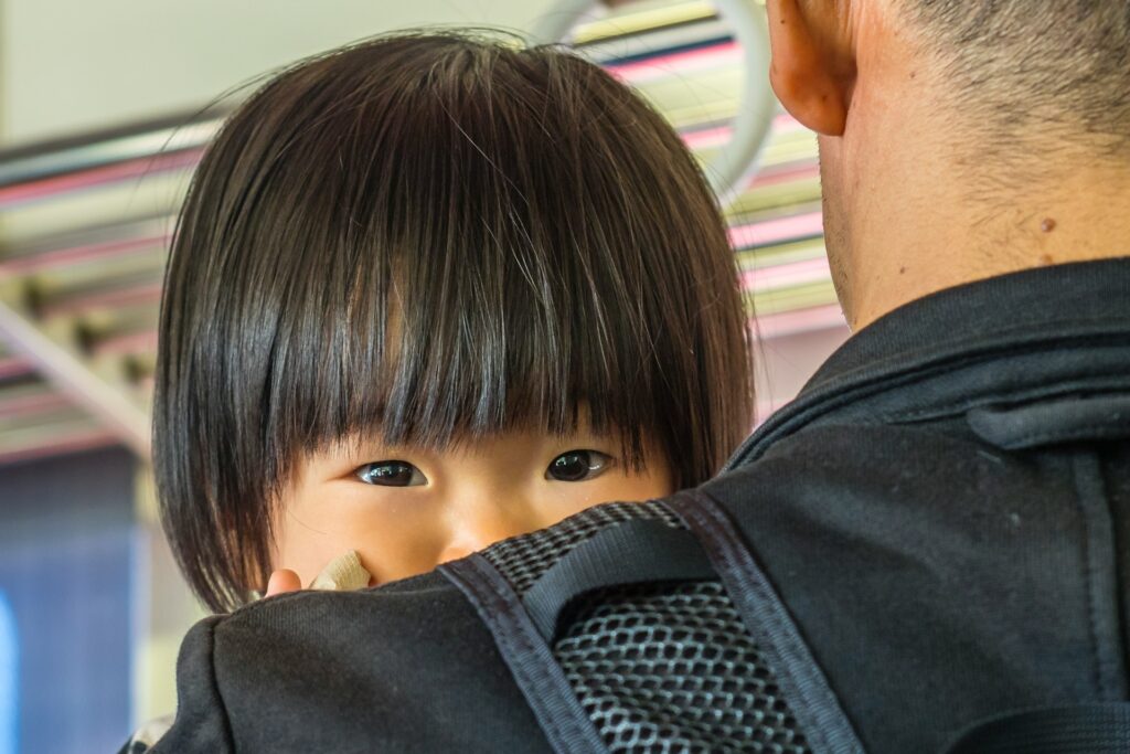 Small child looking at camera over man's shoulder