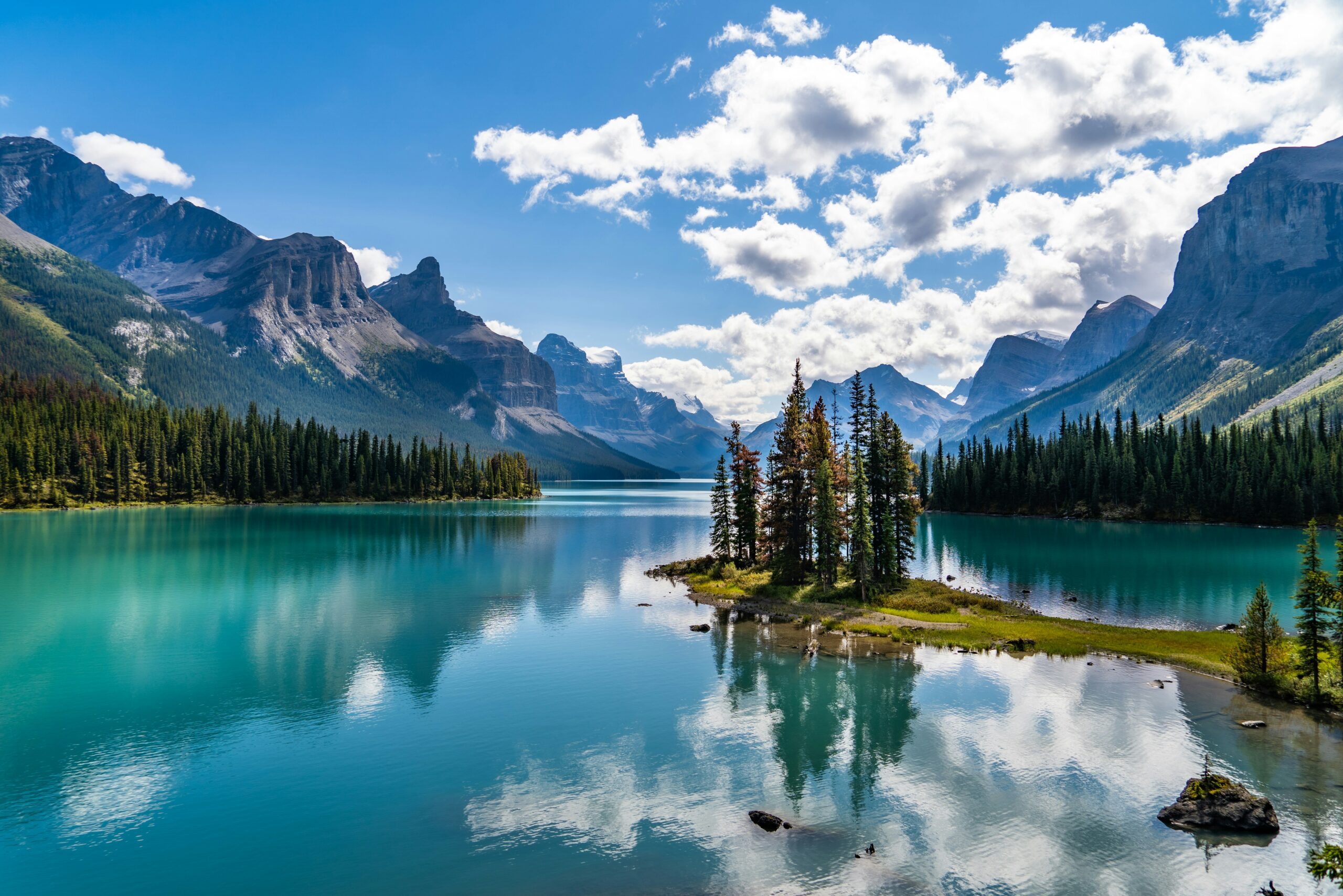 View across bright blue glacial lake, with a tree-covered islet in the centre