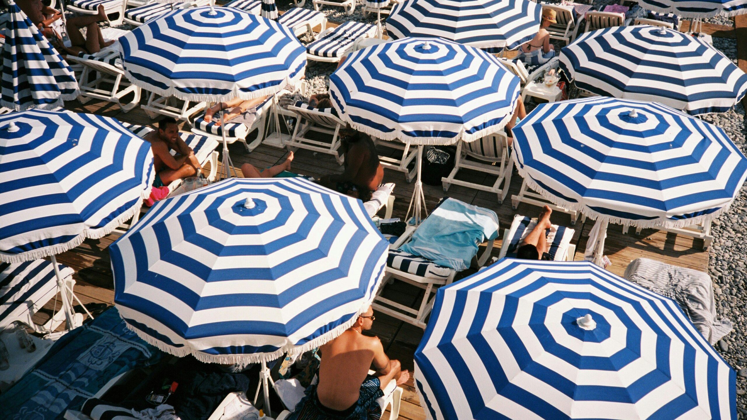 Blue and white striped parasols on a pebbled beach.