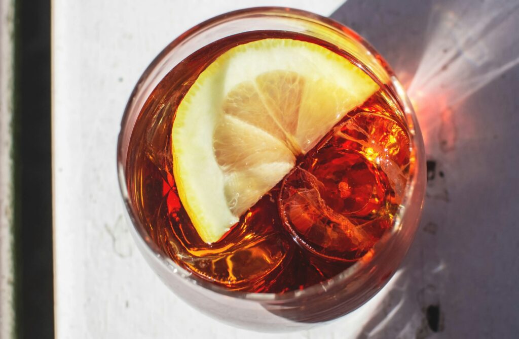 Close up top-down photo of a drink of red liquid with ice cubes and lemon