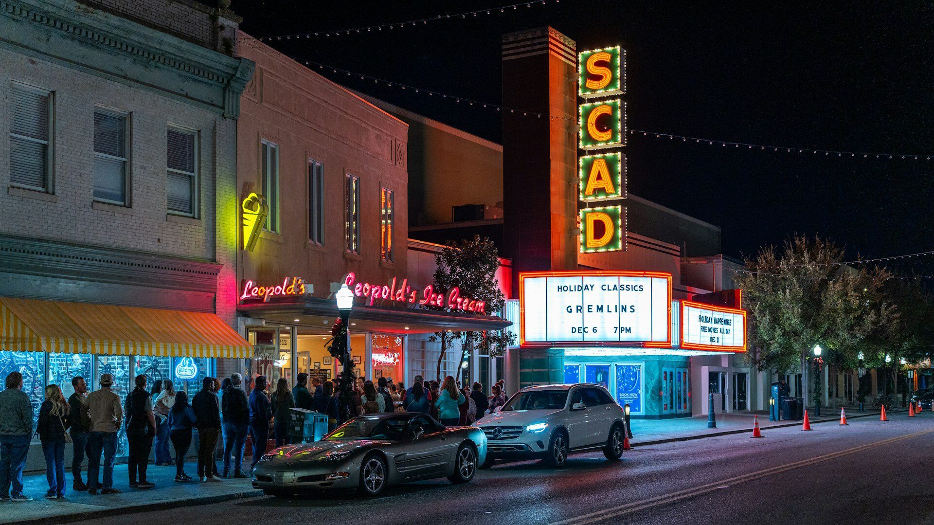 A line of people wait outside an ice cream parlor lit up with neon lights at night