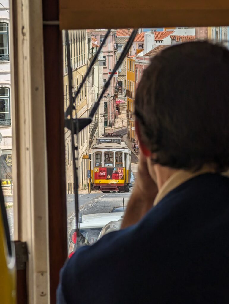 Looking over a passenger's shoulder down a steep street through the front windshield of a Lisbon tram.