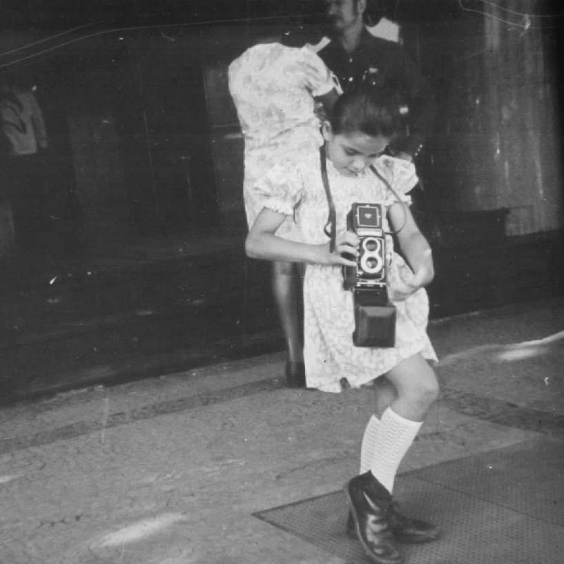 Black and white photo of Dora as a young girl, holding a Roleiflex camera.