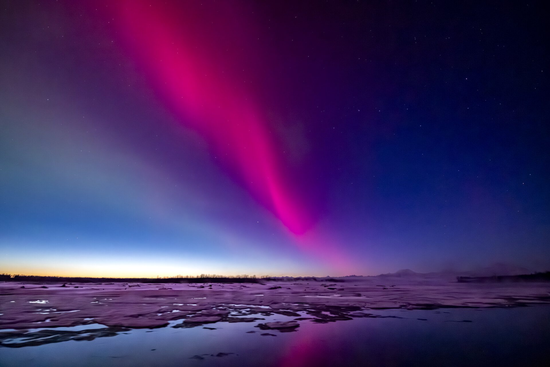 Pink-coloured northern lights over a frozen lake