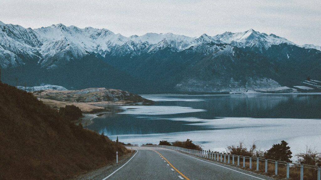 A road leading down to waterfront with snowy mountains in the distance