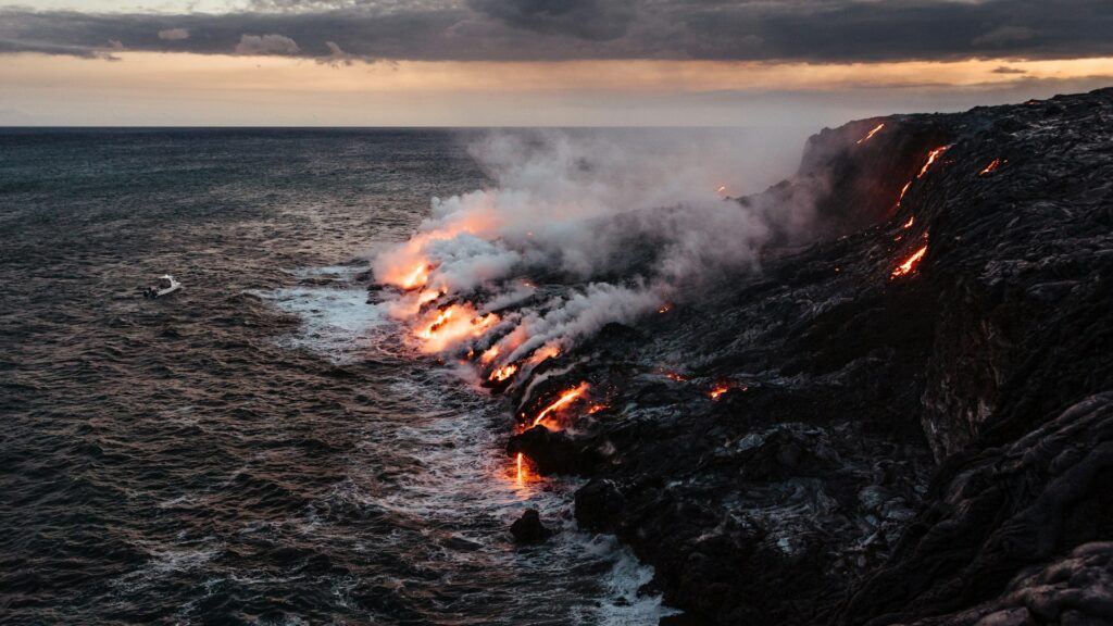 Lava running off a cliff edge into the sea, creating plumes of steam