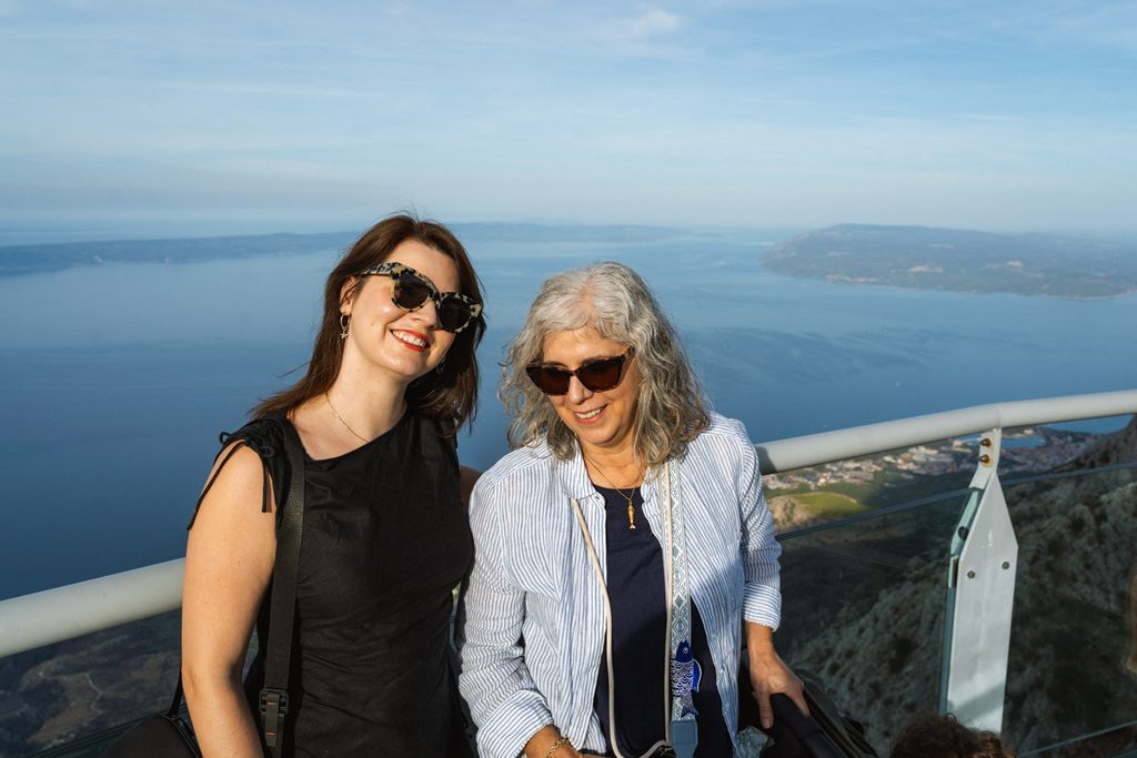 Two women standing at the top of a viewpoint overlooking a Mediterranean archipelago.