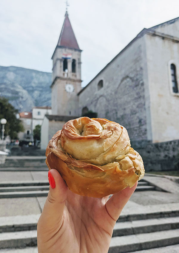 A close up of a hand holding a traditional Croatian pastry, with a church in the background.