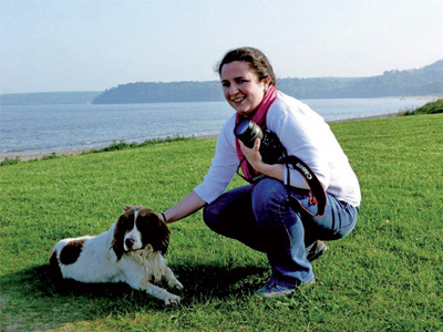A woman kneeling down next to a dog on a grassy field.