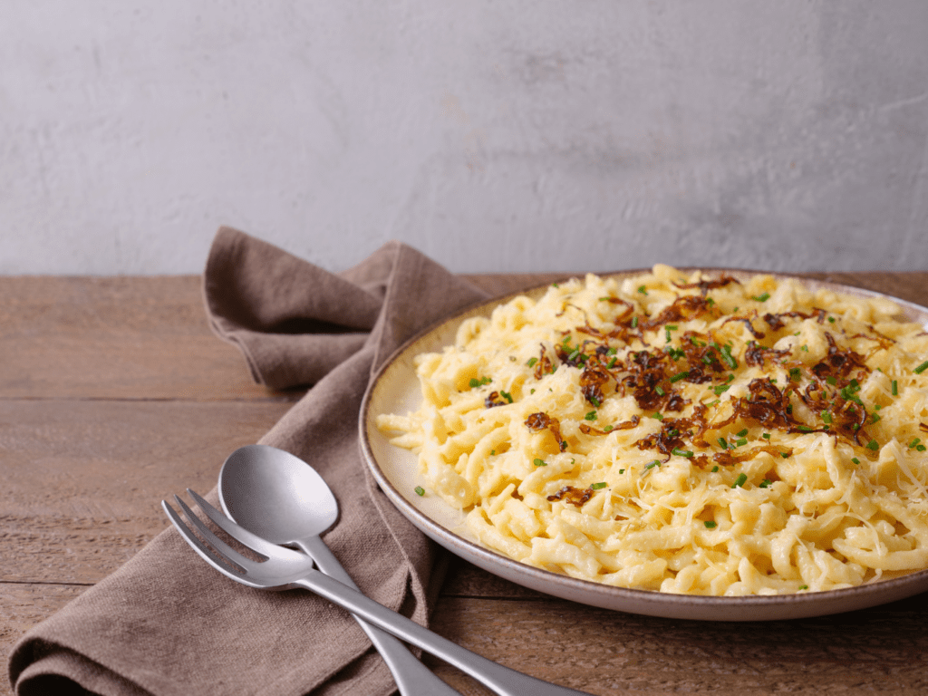 Dish of Käsespätzle on a table with spoon and fork