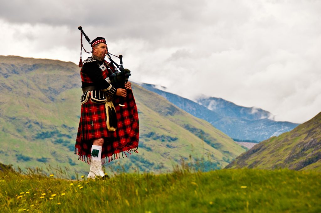 man playing bagpipes in the Scottish Highlands