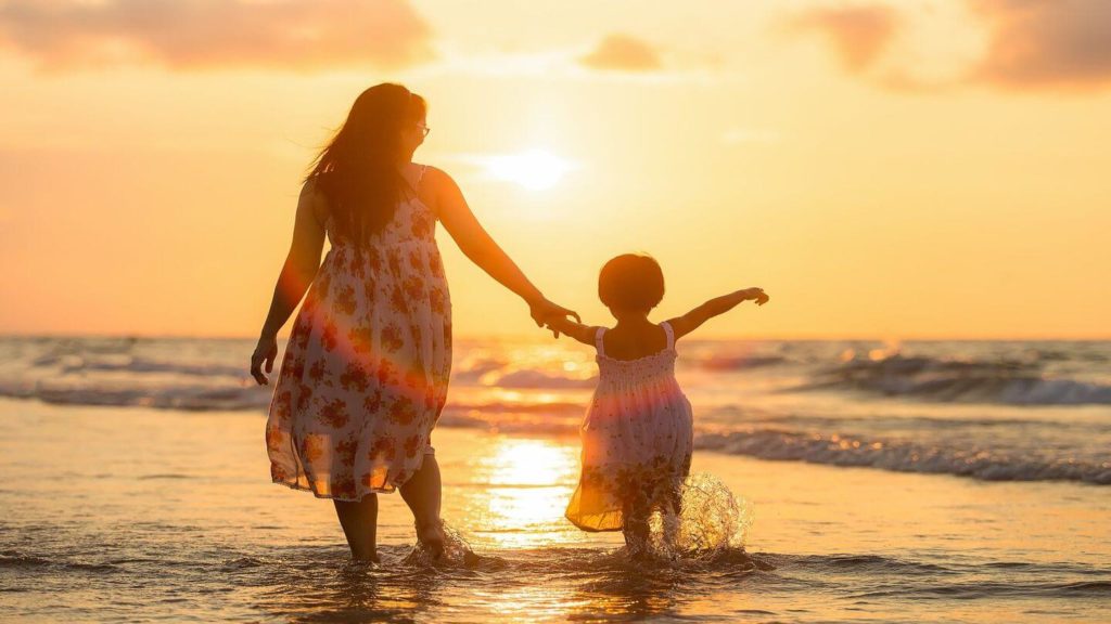 adult and child splashing in the ocean at sunset