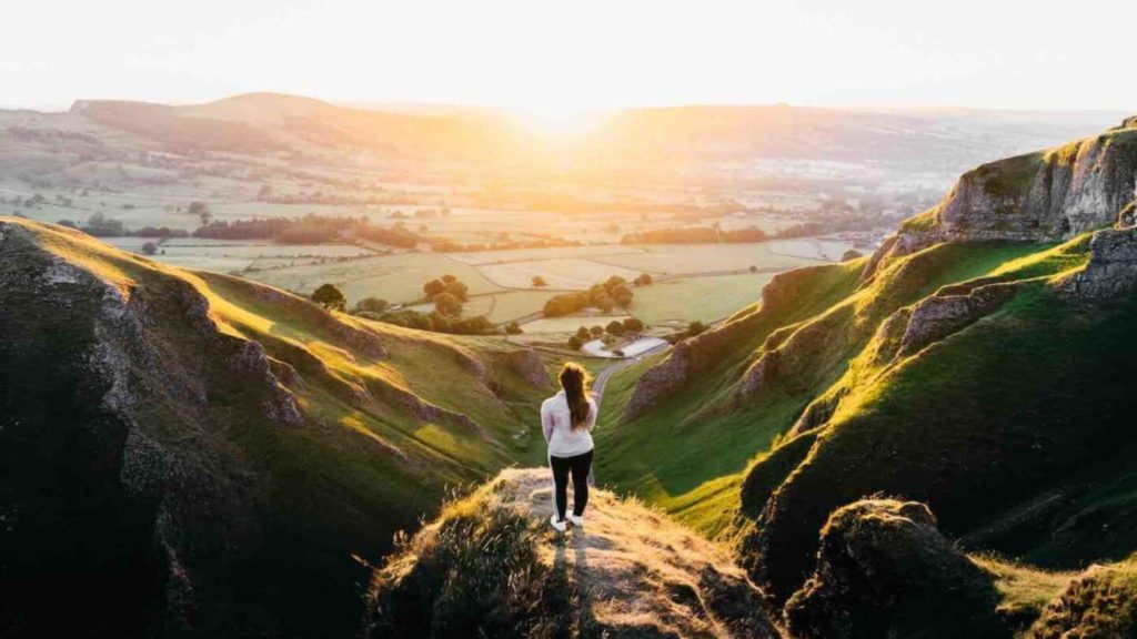 woman standing on mountain viewpoint overlooking green fields