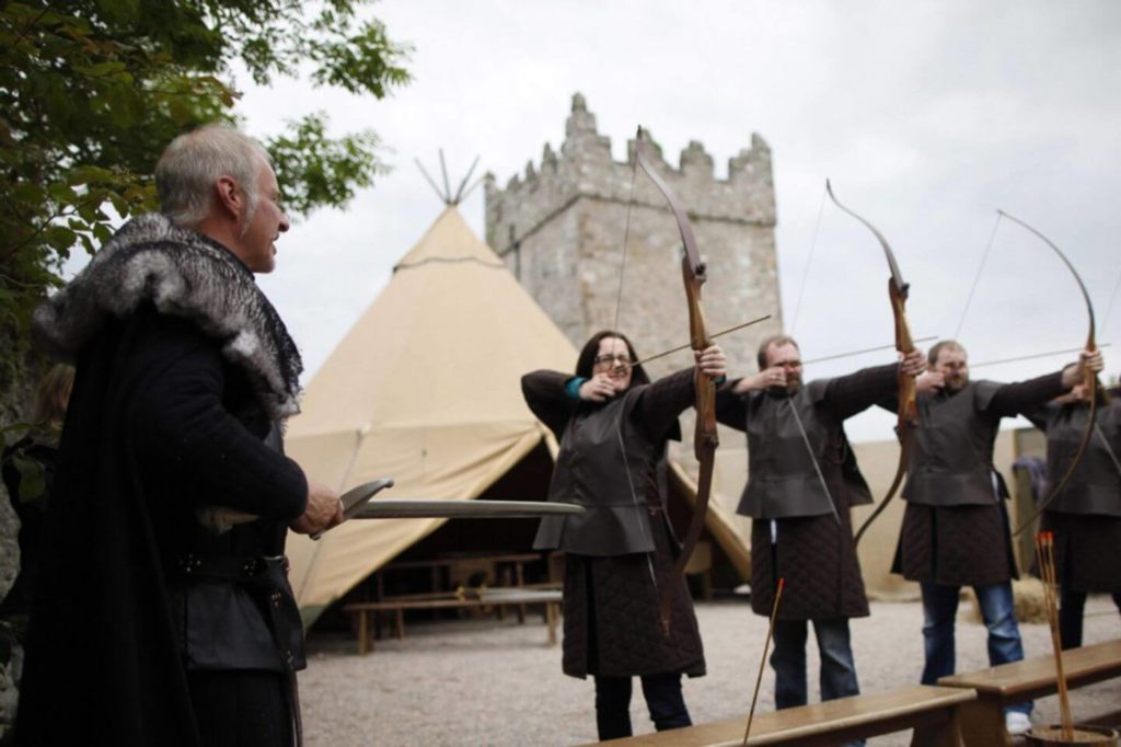 A group of men with bows and arrows in front of a teepee during a family gathering.