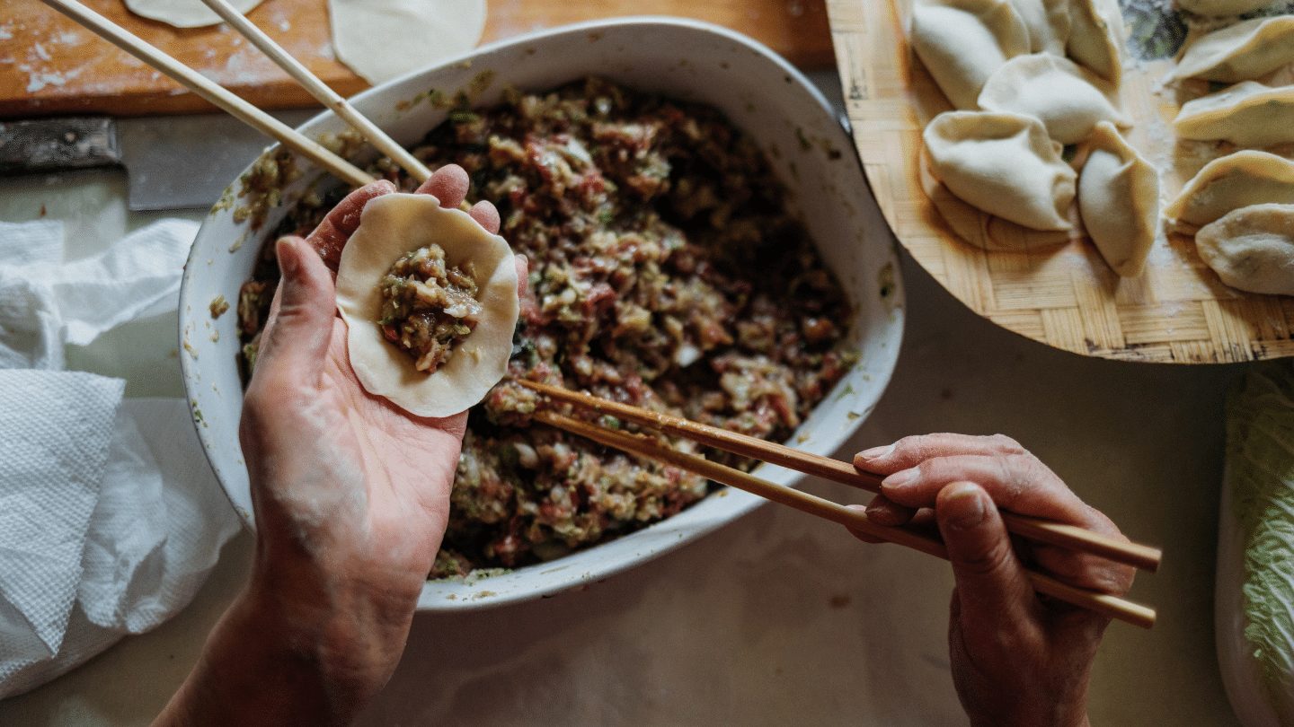 hands stuffing a dumpling with chopsticks - chinese dining experience