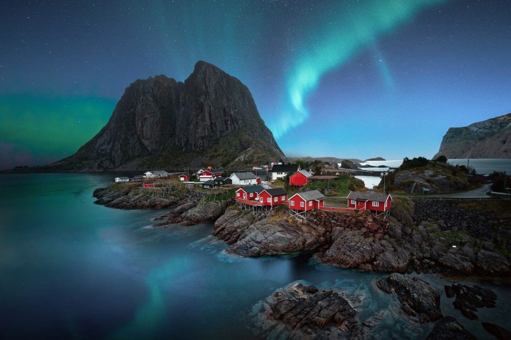 red cottages Northern Lights over rocky coastline Norway