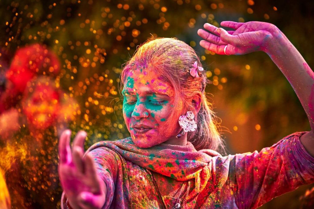 A woman covered in powered paint dancing outside at Holi festival.