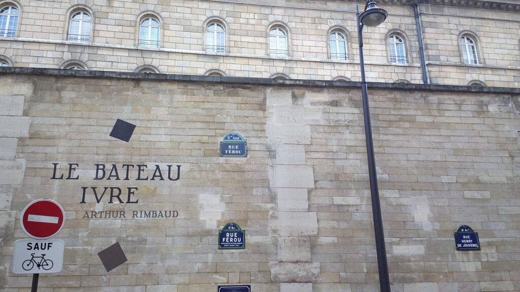 Wall with 'Le Bateau Ivre' written on it in black, underneath it says 'Arthur Rimbaud.' Other plaques are on the wall too, including small blue ones which say 'Rue Ferou.'