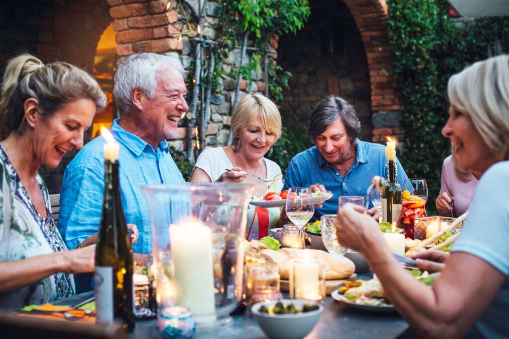 A group of smiling adults enjoying an outdoor dinner party at dusk, celebrating friendships after retirement.