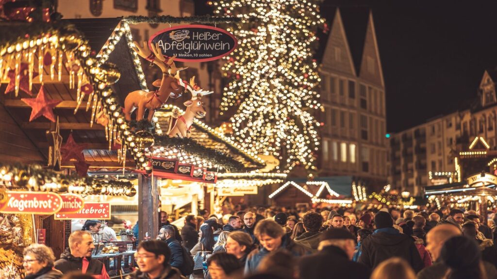 A bustling Christmas market at night, filled with festive decorations and a sign advertising hot apple wine, offers female travel tips for a secure and enjoyable holiday experience.