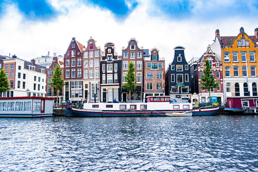 Easter holiday destinations in Europe feature colorful Dutch buildings with distinctive gabled facades overlooking a canal with moored houseboats in Amsterdam.