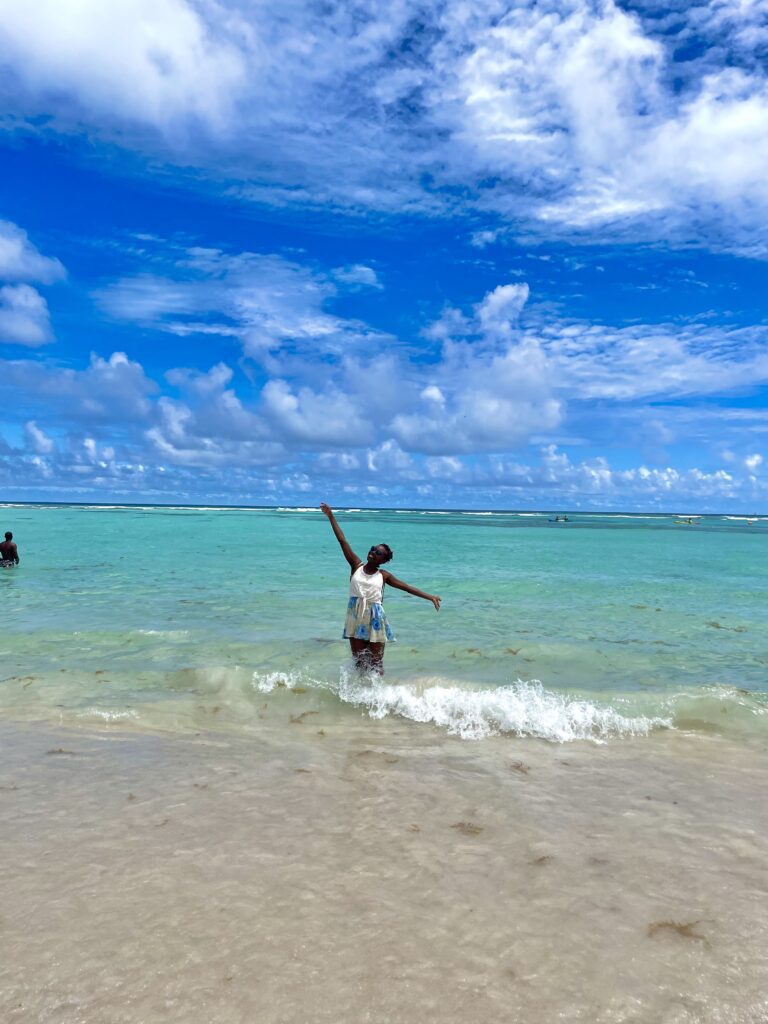 A happy woman with her arms outstretched on a beautiful beach in Barbados.