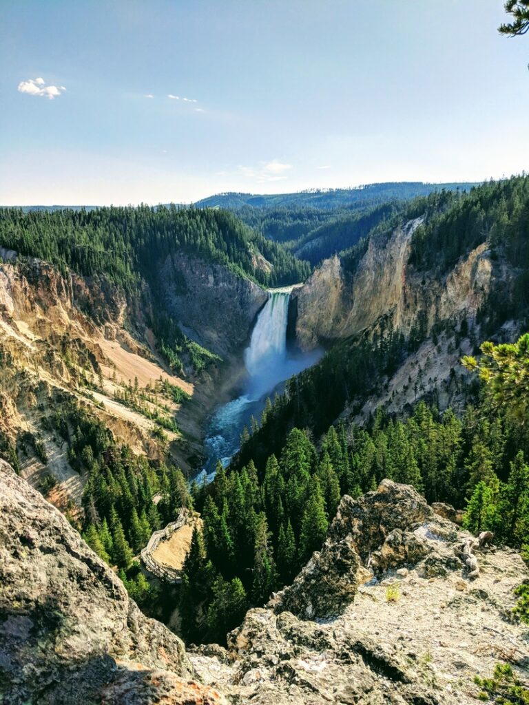 Image of a waterfall at Yellowstone National Park, surrounded by rocky hills and pine trees