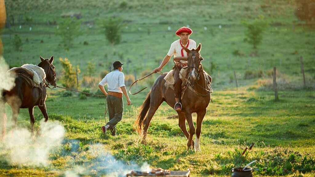 Argentinian cowboys - one on a horse looking to camera, and the other on foot, leading his horse into the distance