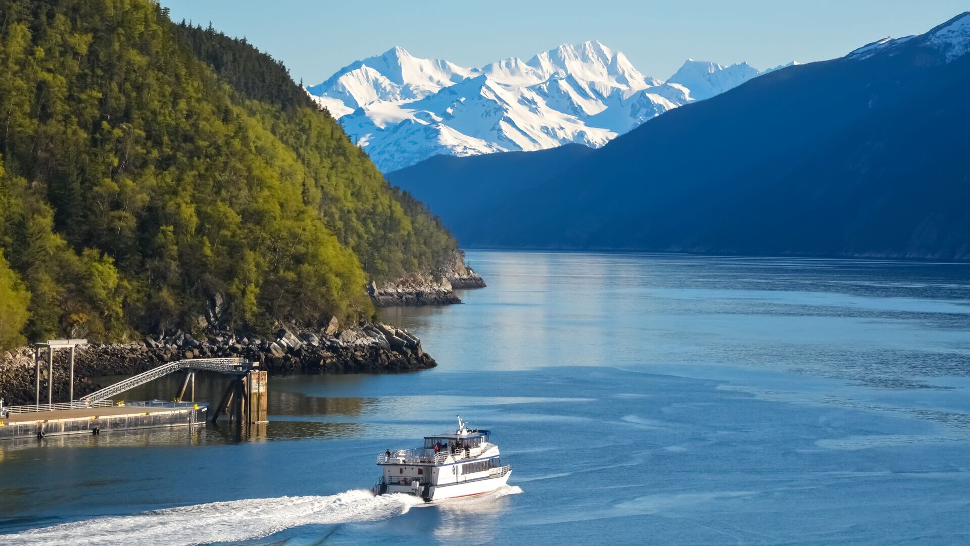 A lake in Alaska with a boat cruising along, with mountains in the background