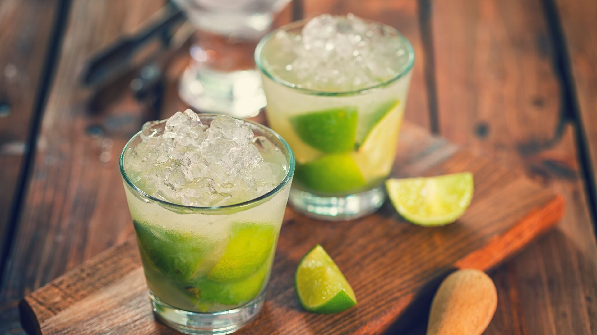 Caipirinhas served on a wooden board, limes around it