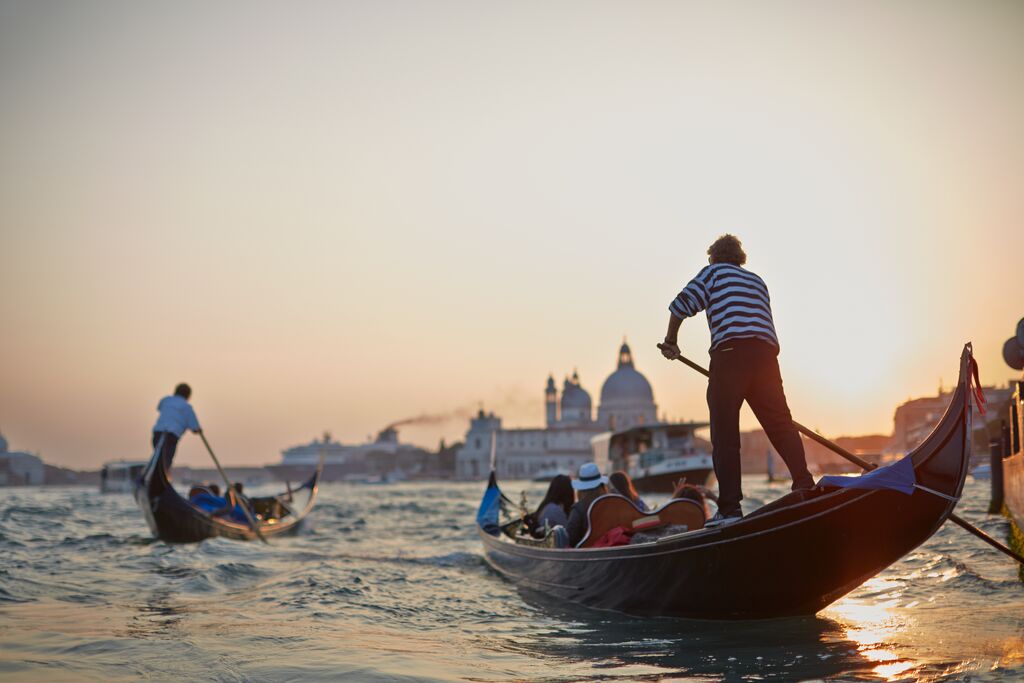 Gondoliers navigate their boats at sunset with Venice, Italy's, historic skyline in the background.
