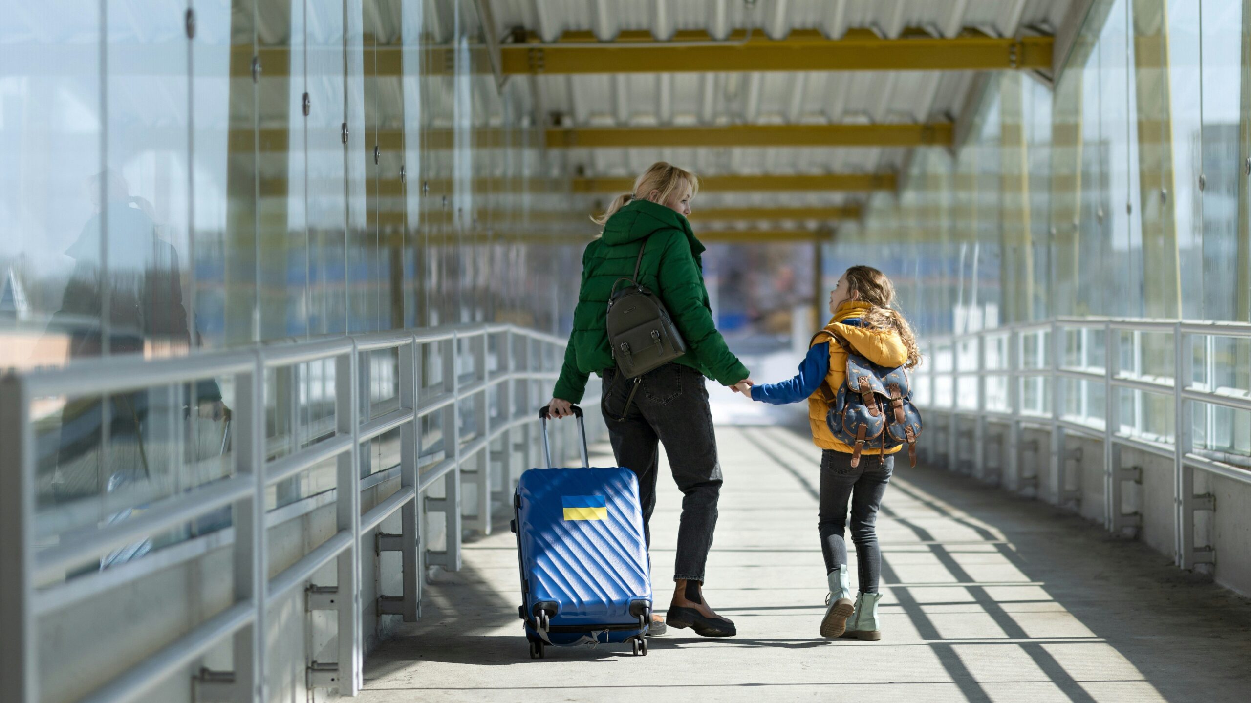 mother and child walking through airport walkway with suitcases