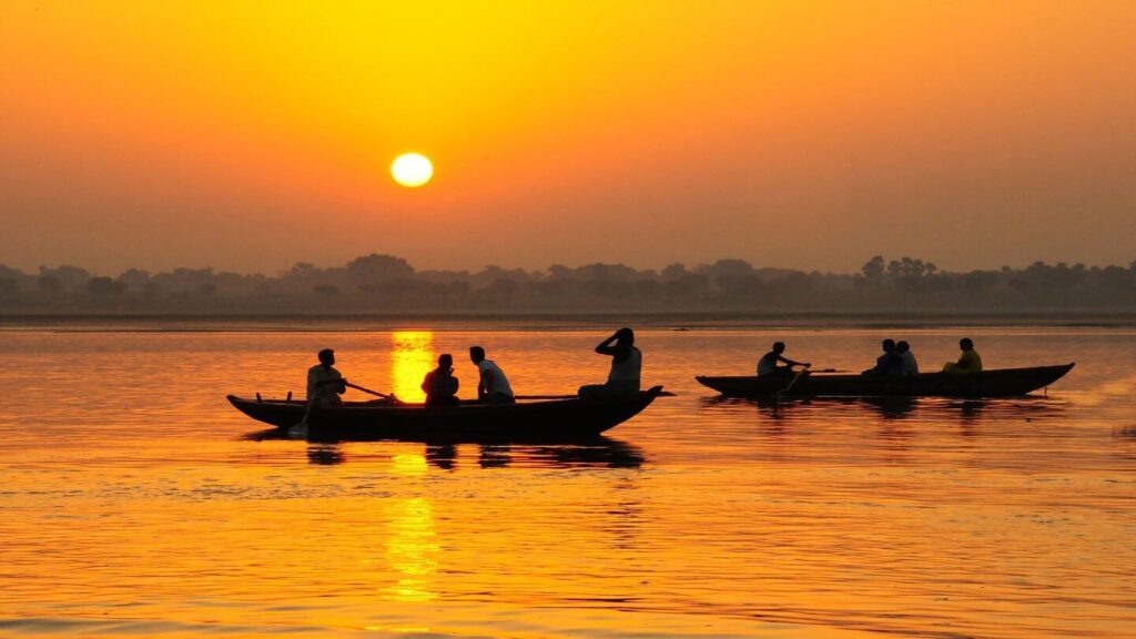 Sunrise over a calm river with silhouettes of people rowing boats, showcasing one of the world’s best river cruises.