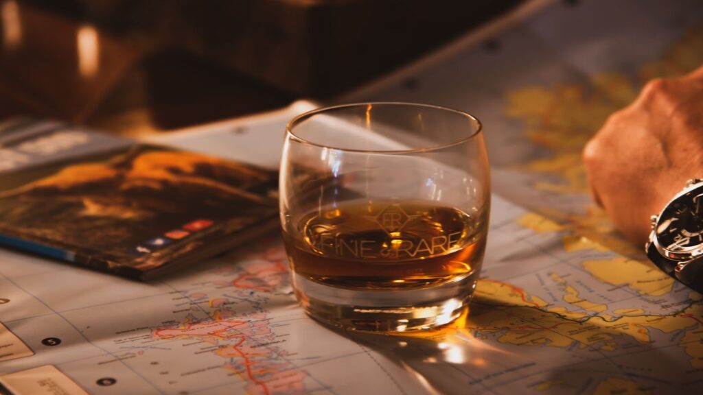 A glass of whiskey on a table with a map and a book about Scottish whisky history in the background.
