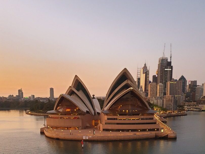 Sunset view of the Sydney Opera House, a popular film location, with the city skyline in the background, reflecting golden hues on the water.