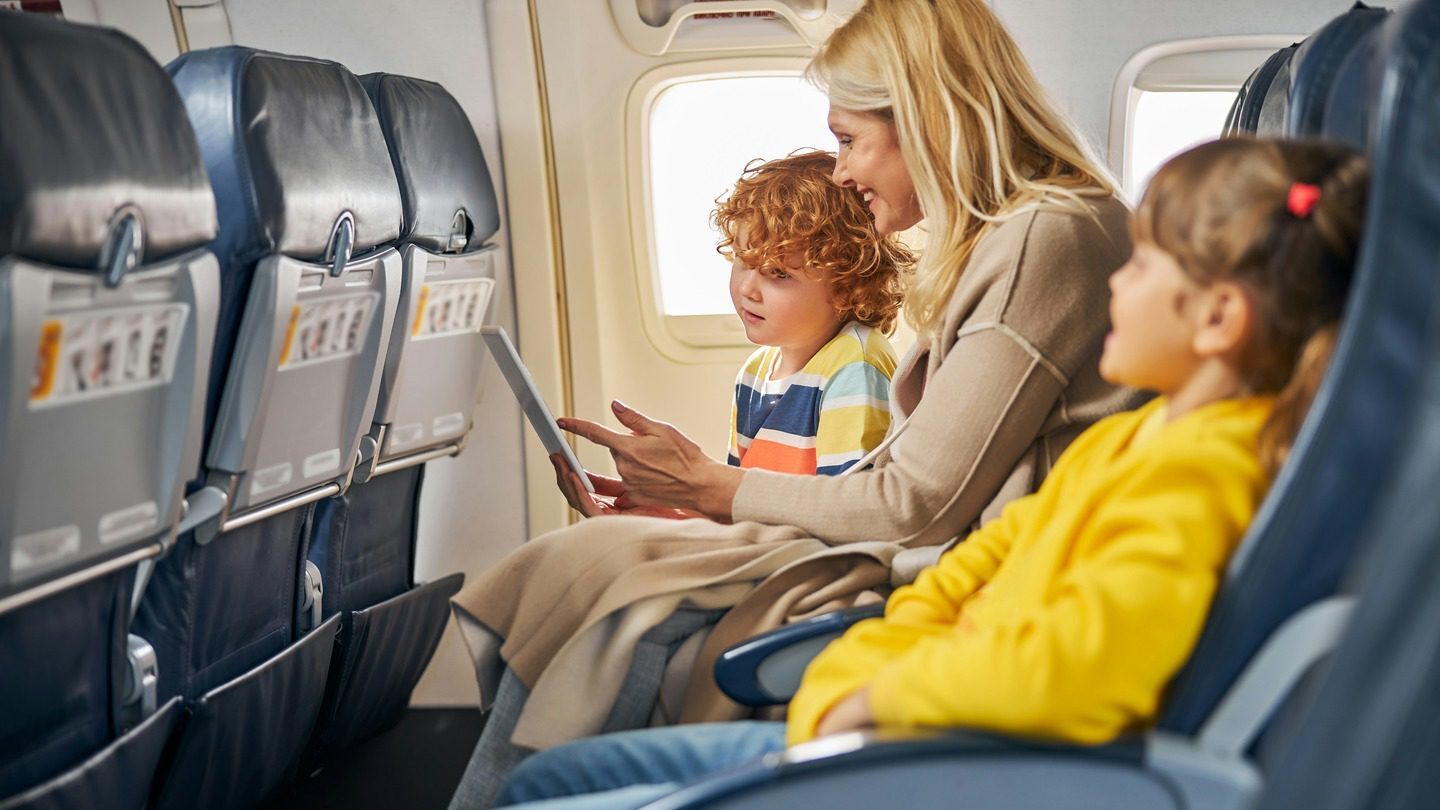 Woman and two children looking at a tablet on board an airplane